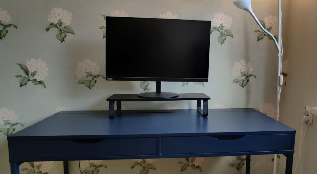 A blue desk with a black display stand and a 27" ThinkVision display on top
