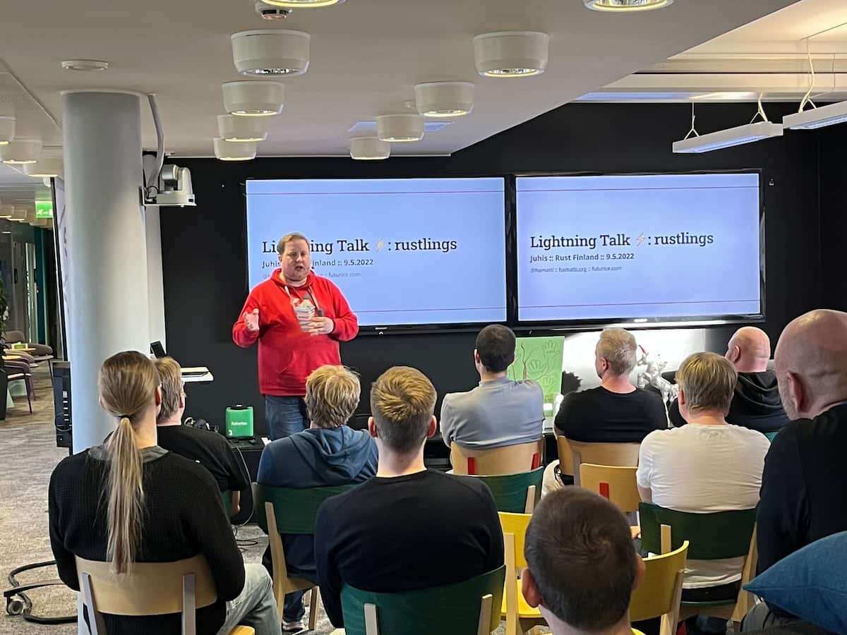 Me doing a talk in front of a small audience at Futurice office with slide behind me saying "Lightning talk: rustlings"
