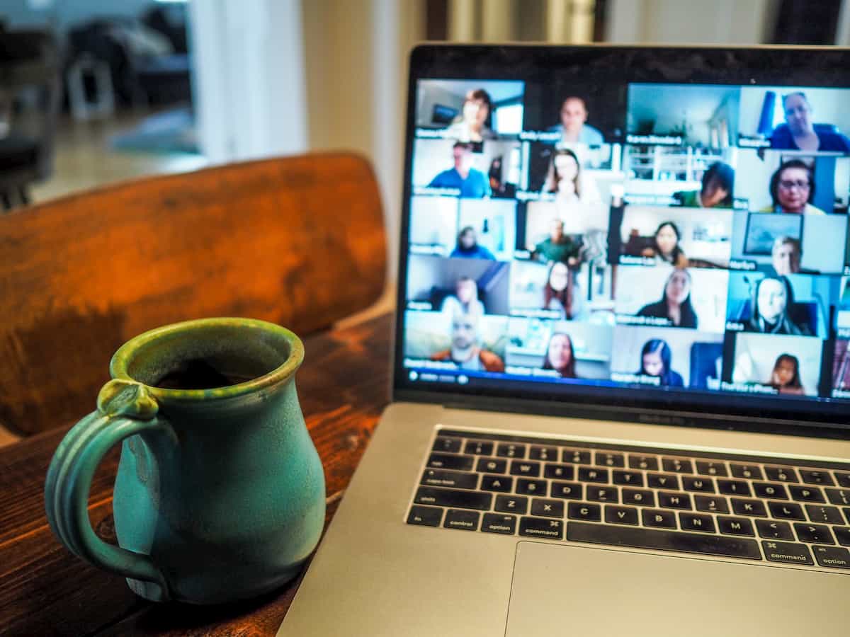 A video conference on a laptop and a maroon coffee mug next to laptop