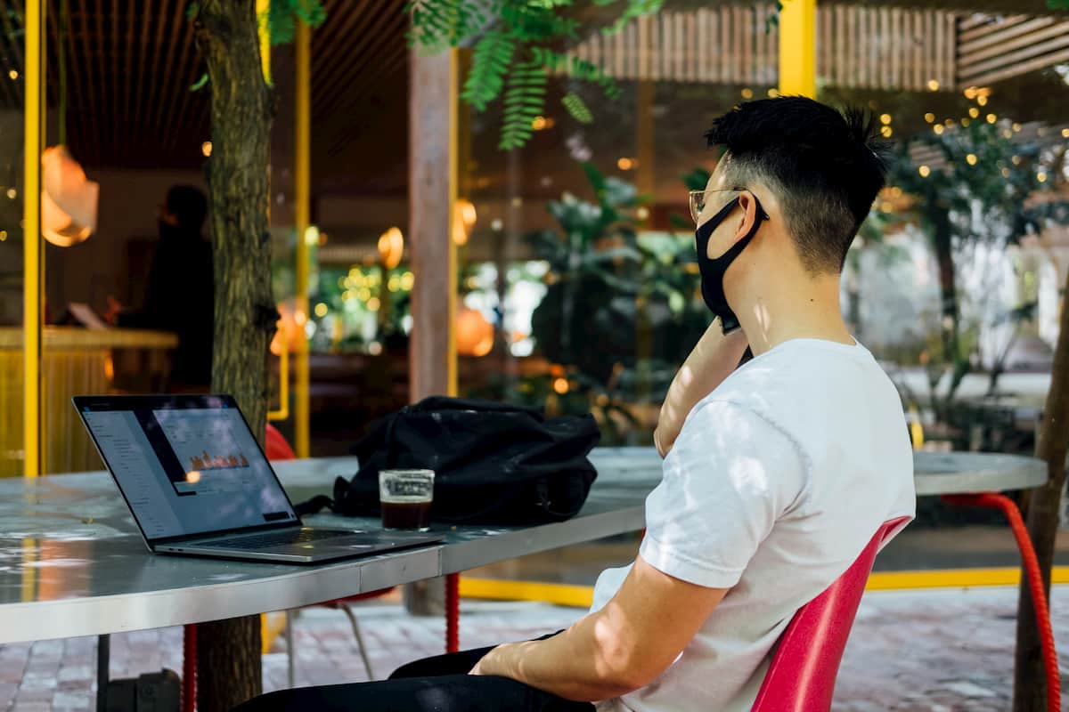 Man wearing a mask sitting in a cafe with a laptop