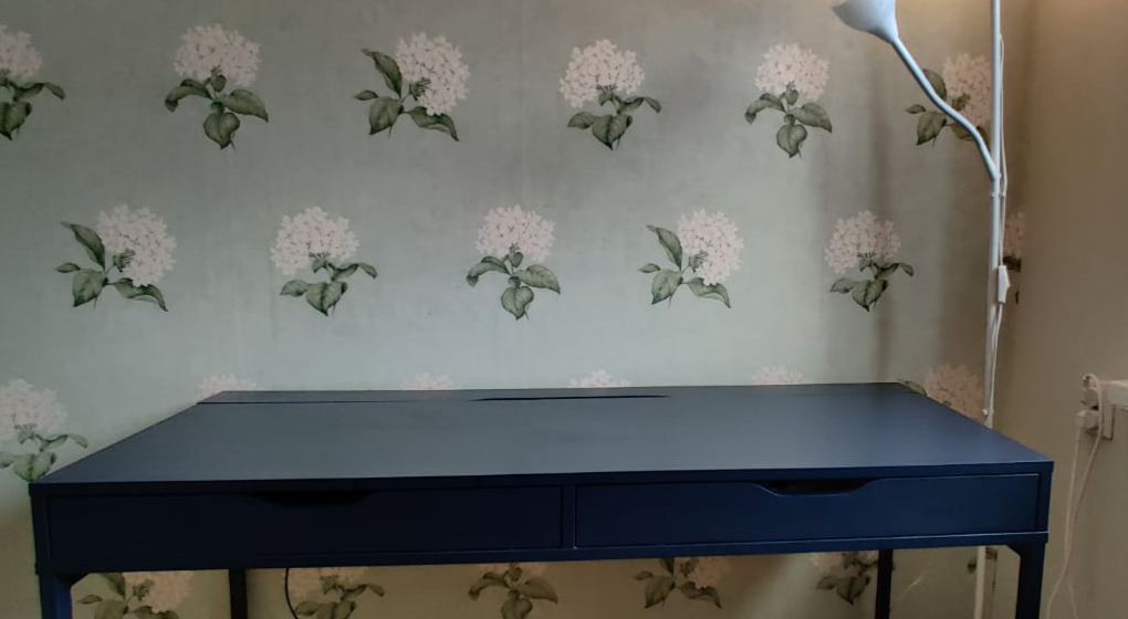 An empty desk with two drawers in front of a flower wallpaper