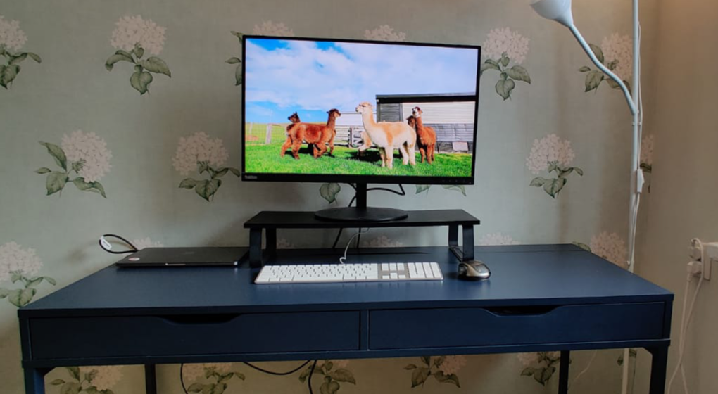 A desk with closed macbook connected to a display, white keyboard and black/grey mouse