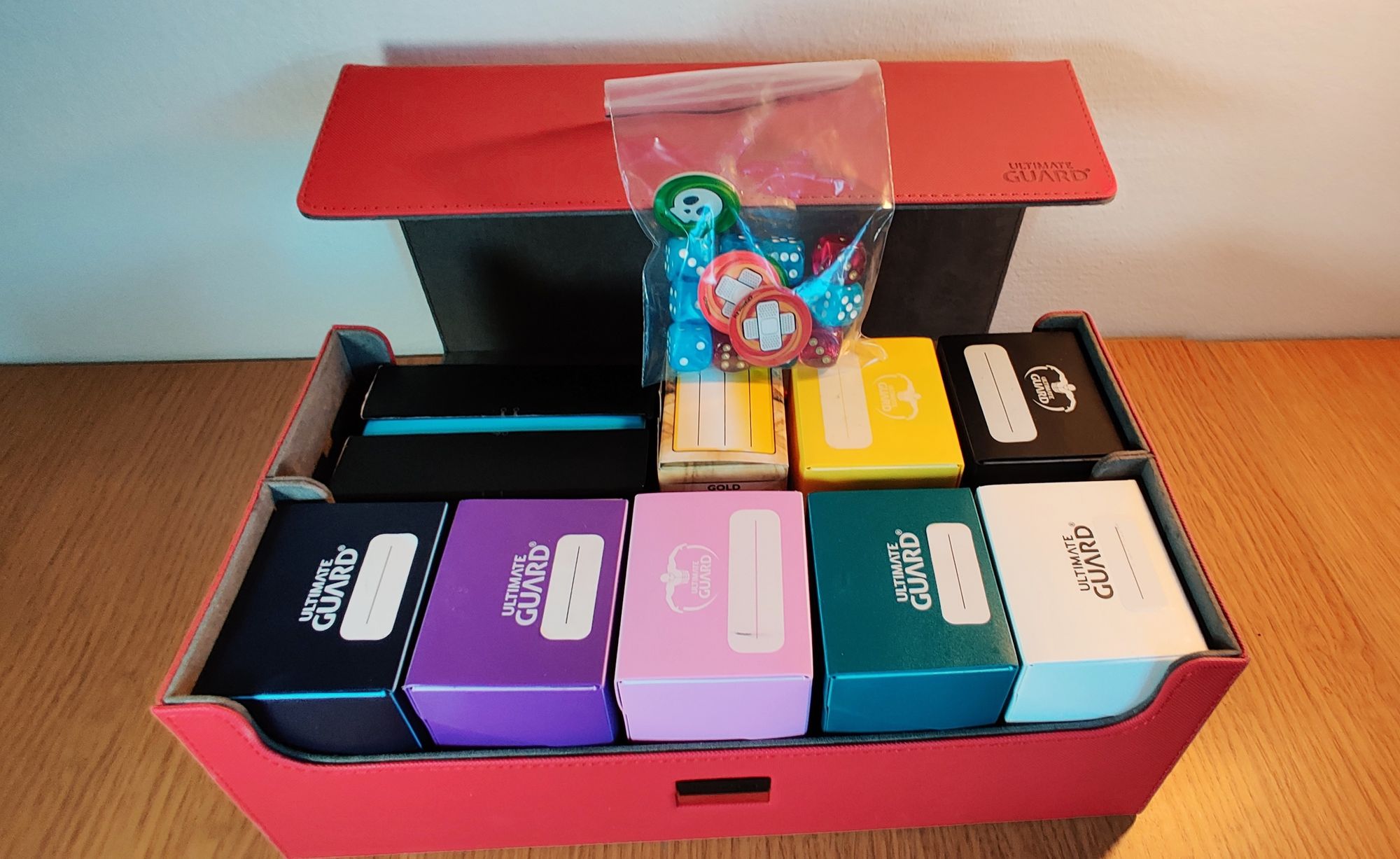 A large red box with open lid and 9 small deck boxes of games inside