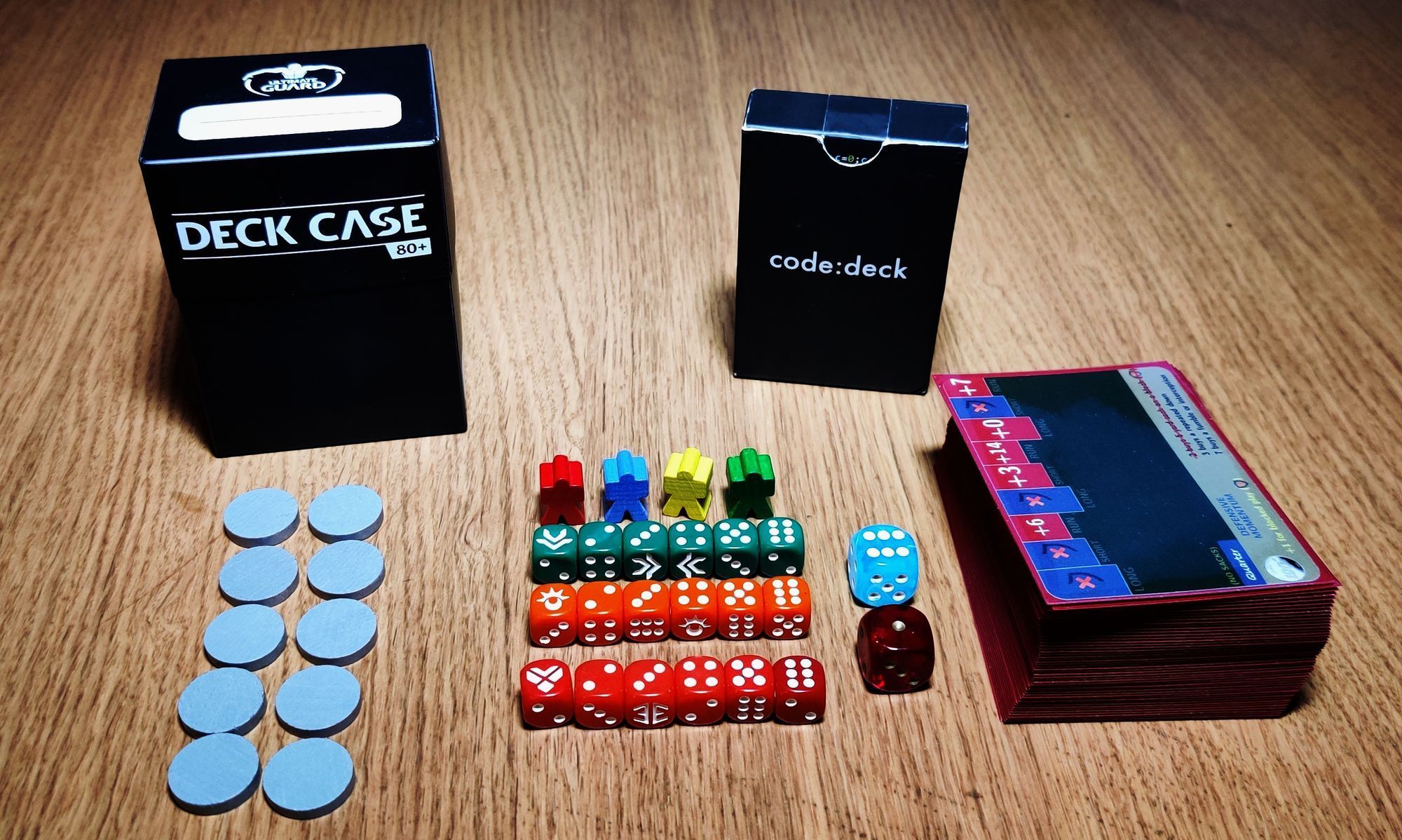A deck box, tokens, meeples, dice and a pile of cards organized in a beautiful symmetry on a wooden table