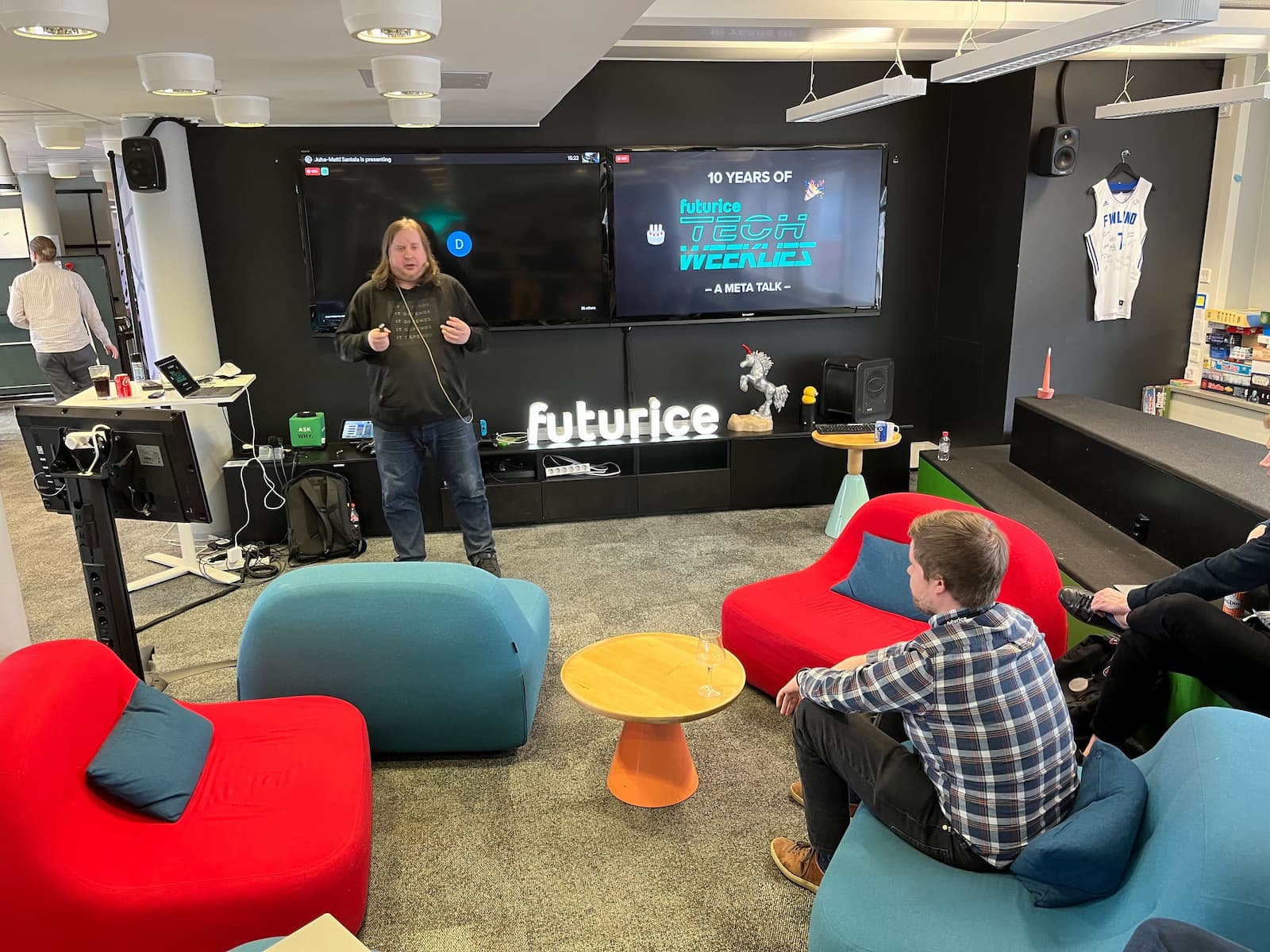 Me on a stage in front of small developer audience, wearing a headset and "It depends" hoodie. A slide behind me says "10 years of Futurice Tech Weeklies" with a few party emojis.