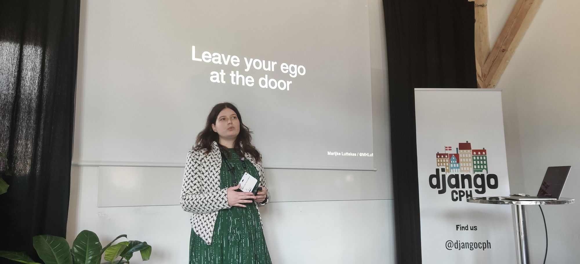 Marijke speaking on stage with a slide about leaving your ego at the door