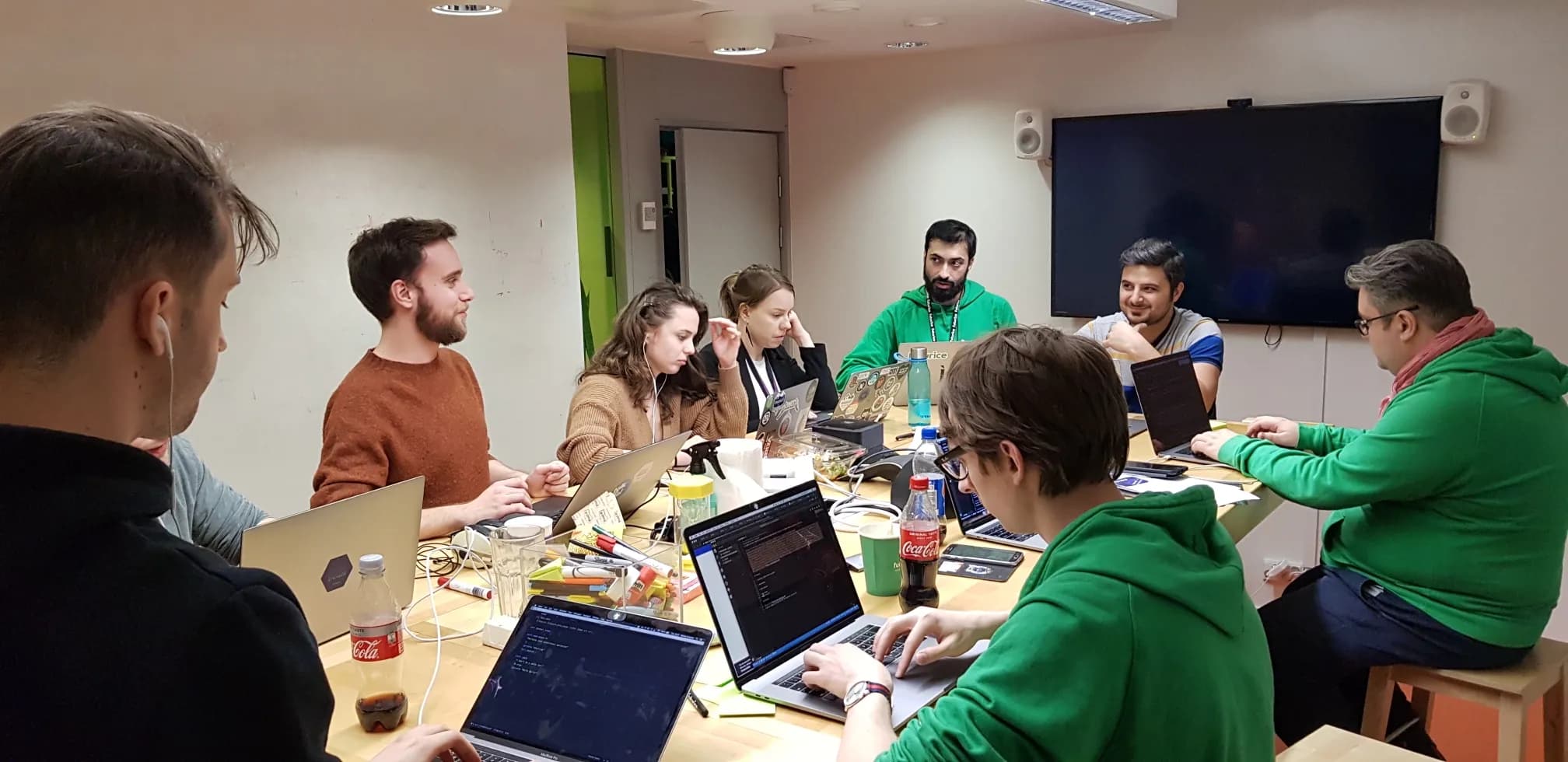 A group of developers in a meeting room, around a table, working on their laptops and discussing