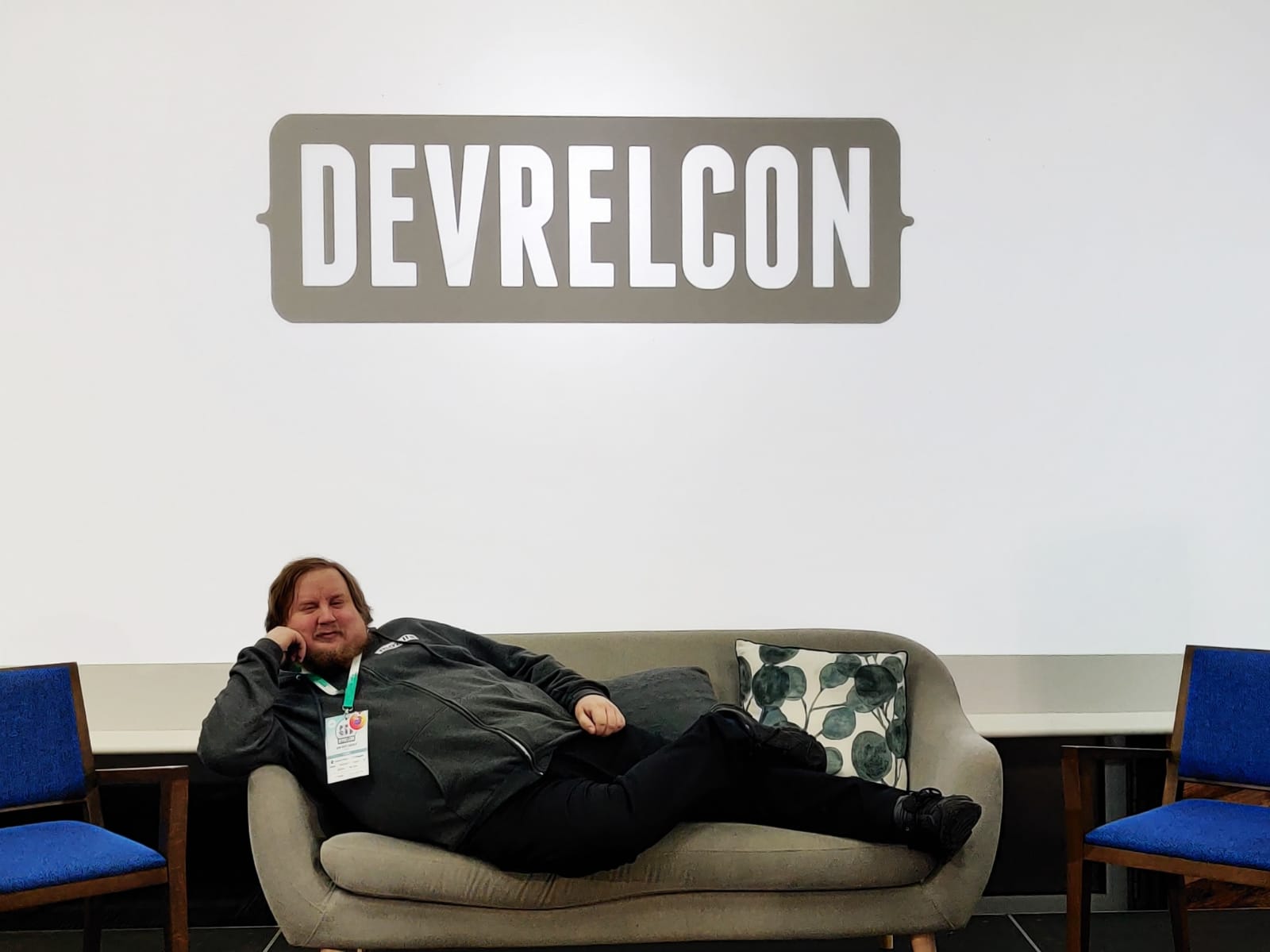 Juhis on lying a couch on stage with DevRelCon logo on the large screen behind him