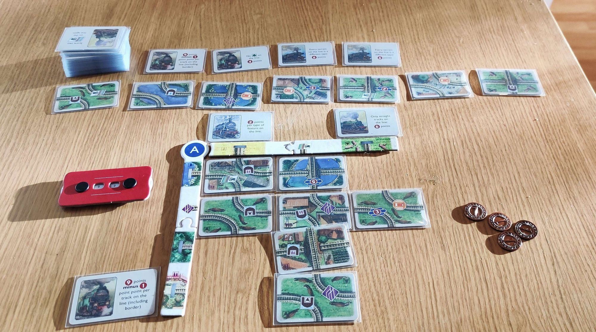 A game play of Village Rails with a partially filled grid of rails, few copper coins and a market of cards next to the play area