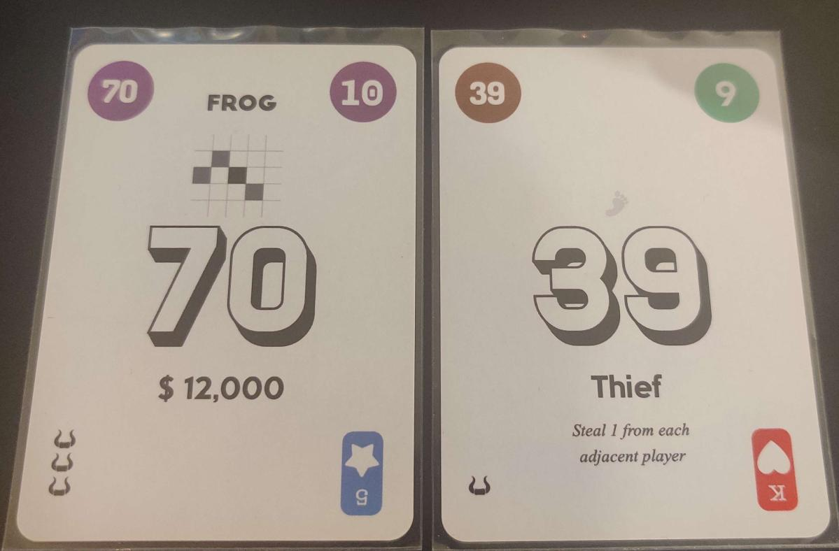 On left, card numbered 70 with Onitama frog pattern, text "$12,000" and three bull heads. On right, card numbered 39 with barely visible grey footprint, text "Thief: Steal 1 from each adjacent player" and 1 bullhead