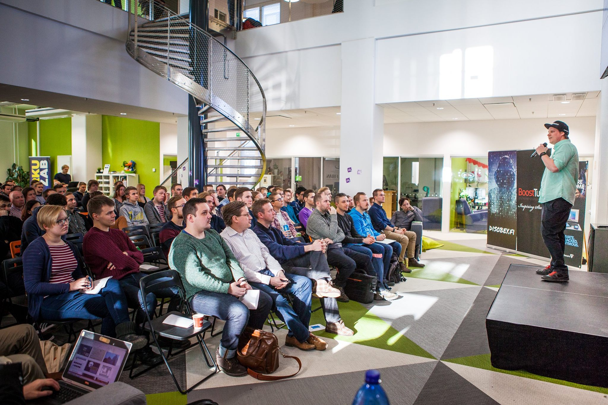 A room full of people sitting, listening to a man on a stage speaking.