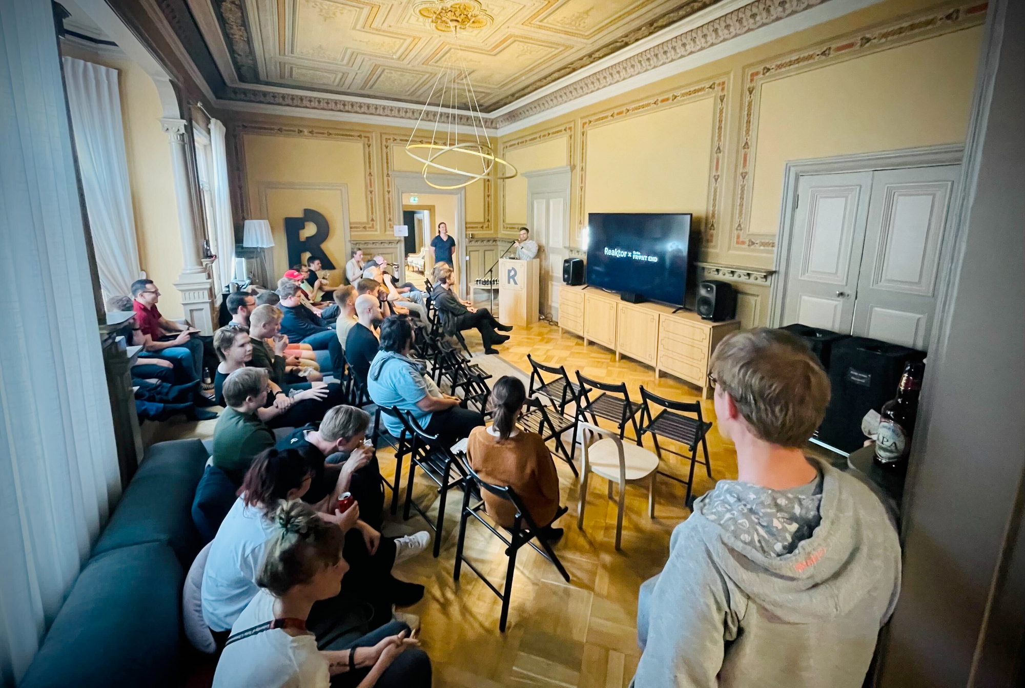 A group of people sitting in rows of chairs, listening to a person speaking in front of the room