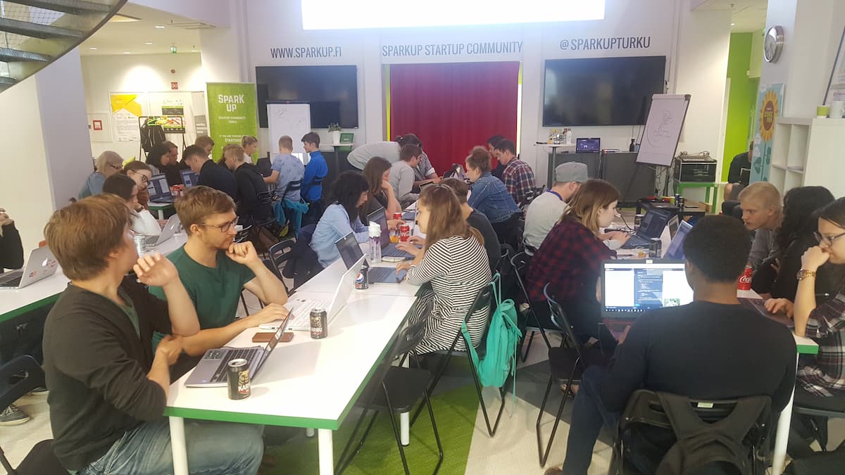 A room full of people with their laptops, some coding on their own, others discussing in small groups
