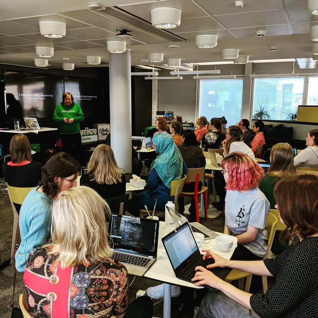 A group of people sitting around tables with their laptops, listening to me speak in front of them in the small auditorium space