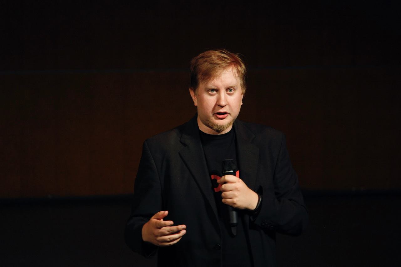 A close-up of me on a stage with a microphone, wearing a suit jacket and Boost Turku t-shirt underneath
