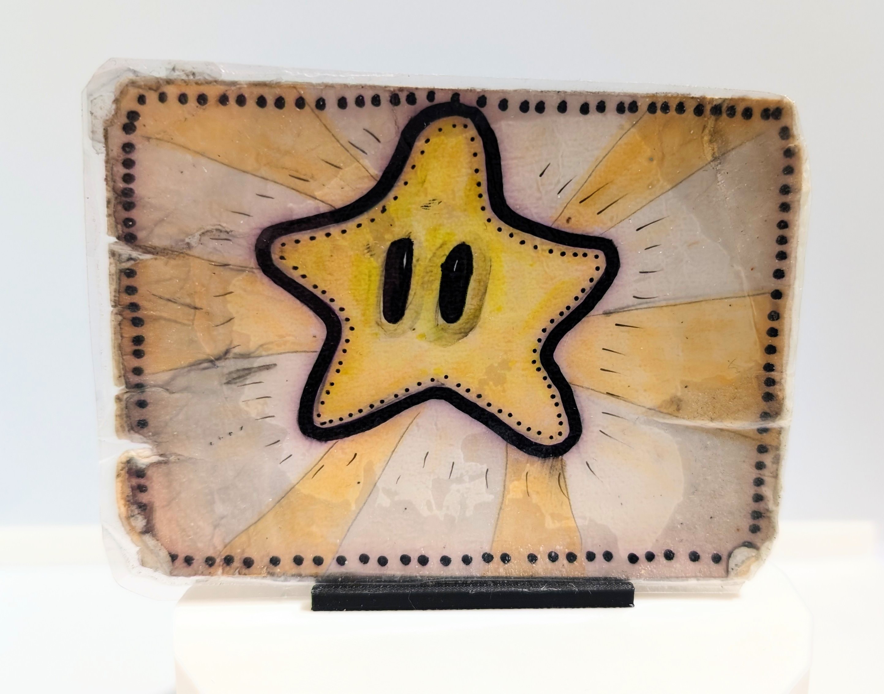 A hand-drawn post card with a Super Mario Super Star. The card has taken a lot of damage on the edges and has become discoloured at parts.