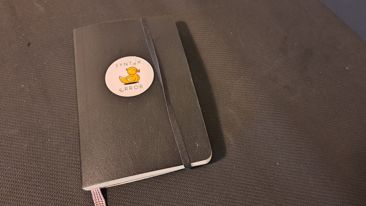 A black small notebook with a rubber duck sticker on the front cover and an elastic band to hold it close 