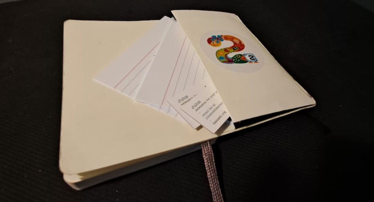 An open notebook with a back pocket and a couple of index cards and business cards halfway out from the pocket. 