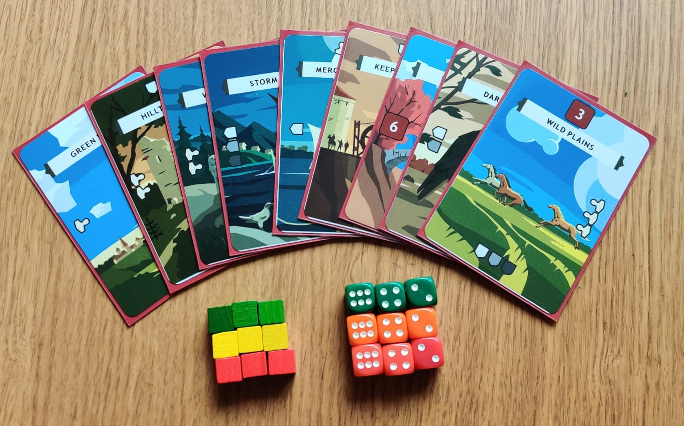 A fan out of nine game cards with illustrated scenery. Next to them, 9 wooden blocks and 9 dice, 3 of each in green, orange and red. 