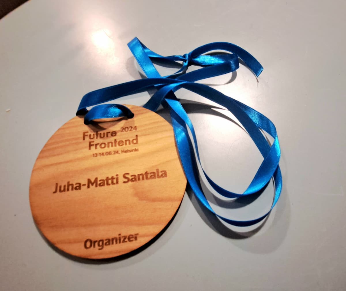 A wooden conference badge with text “Future Frontend 2024 13.-14.6.24, Helsinki; Juha-Matti Santala; Organizer” 