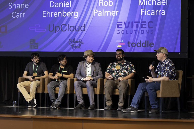 Group of five people on a panel discussion, sitting on chairs on stage 