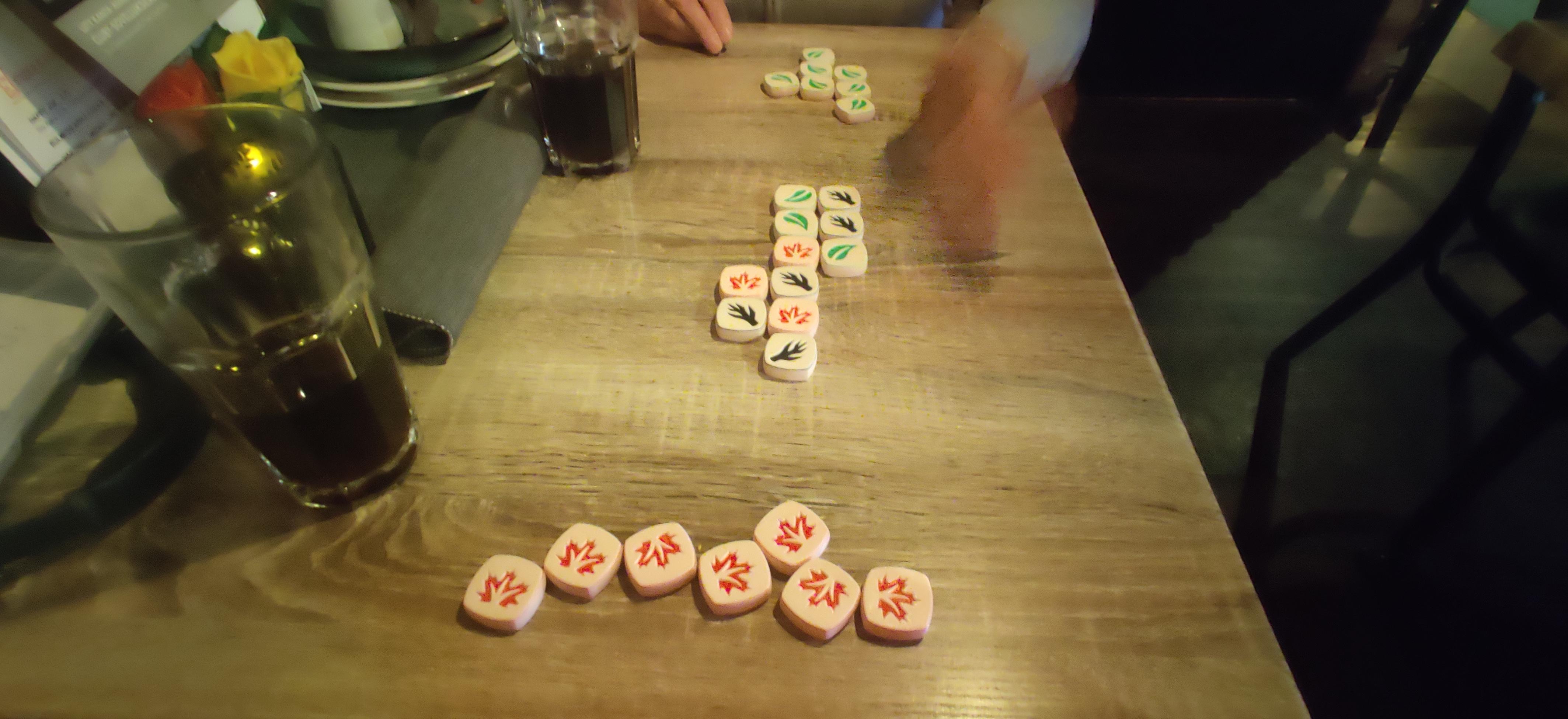 A game of Leaves in a restaurant table with some drinks. In the middle, a dozen tiles are played with both players having a bunch of red and green tiles in front of them. 