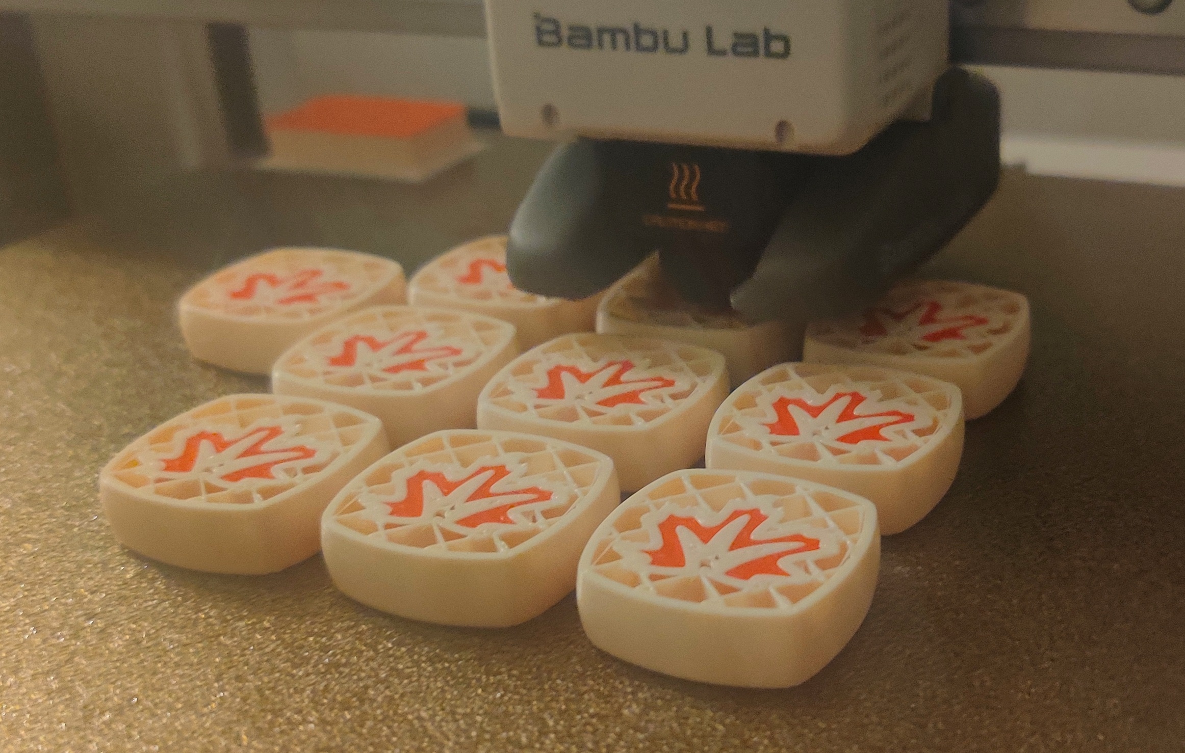 In progress 3D printof thick white square tiles with a bit of red accent color being printed in the middle of each tile to form a maple leaf. 