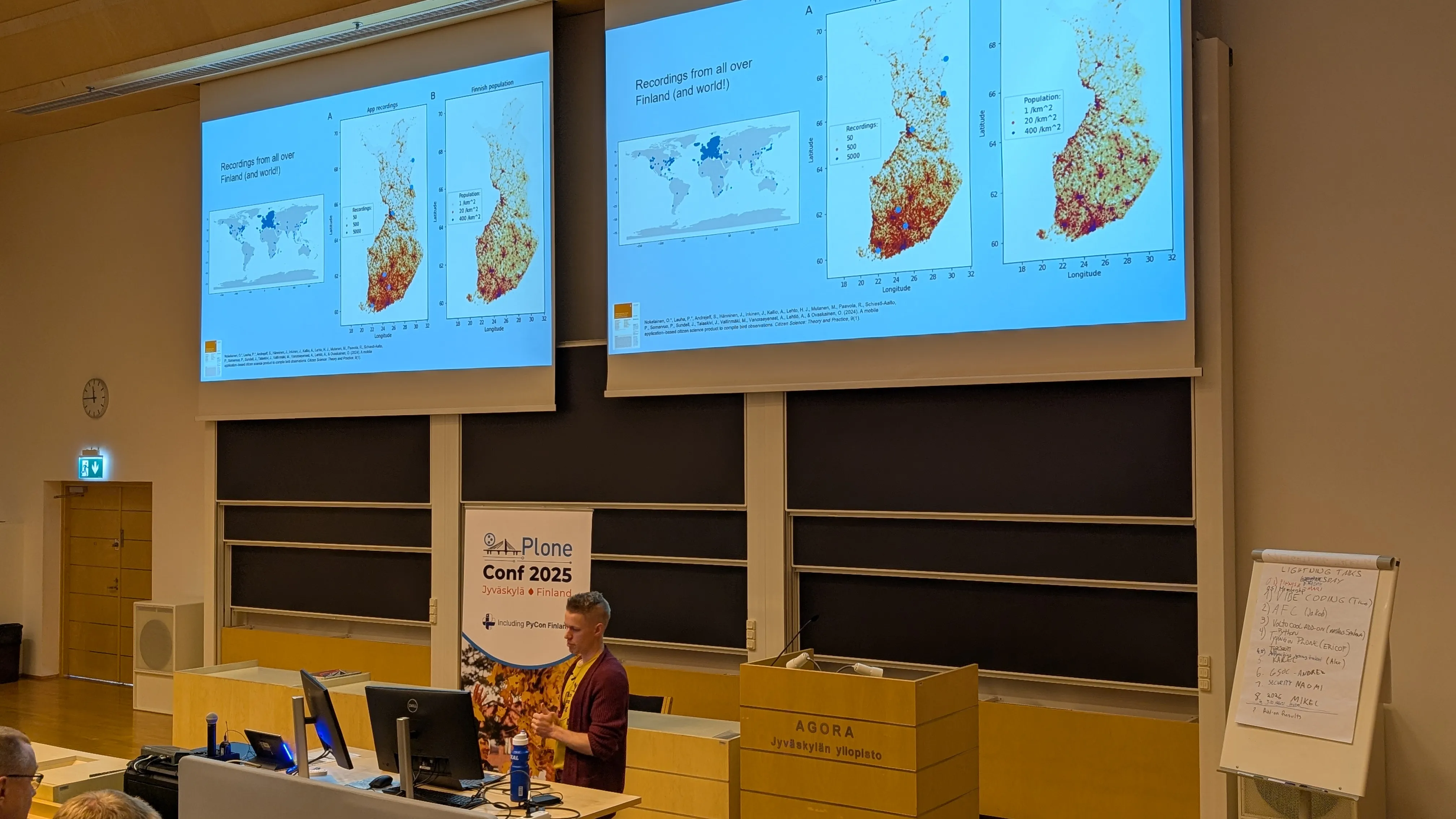 Patrik speaking in front of an auditorium with a slide t hat shows a wolrd map that’s blue in Europe and grey elsewhere and two maps of Finland with mostly red and yellow dots in the south and white in the north.
