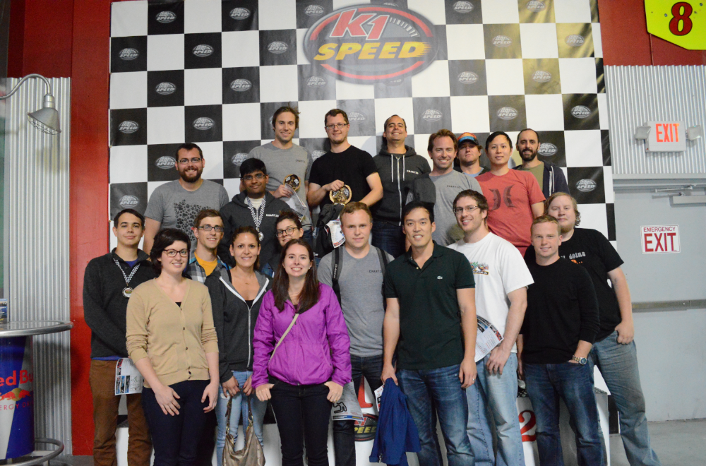A group photo of 20 people standing on a karting podium. 