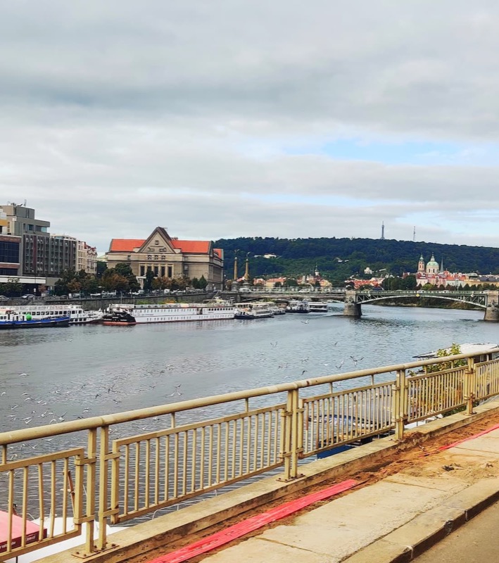 Vltava river photographed from a tram, showing a few beautiful buildings in Prague and the forest hills in the horizon. 