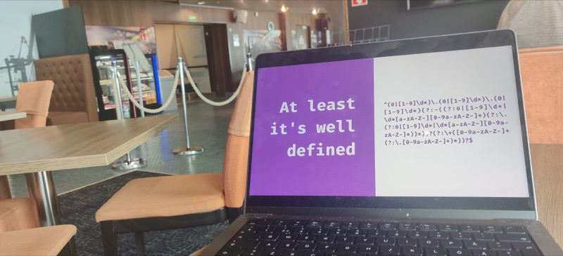A laptop with a slide about regex on it. On the background, a ferry’s pub and empty lobby 