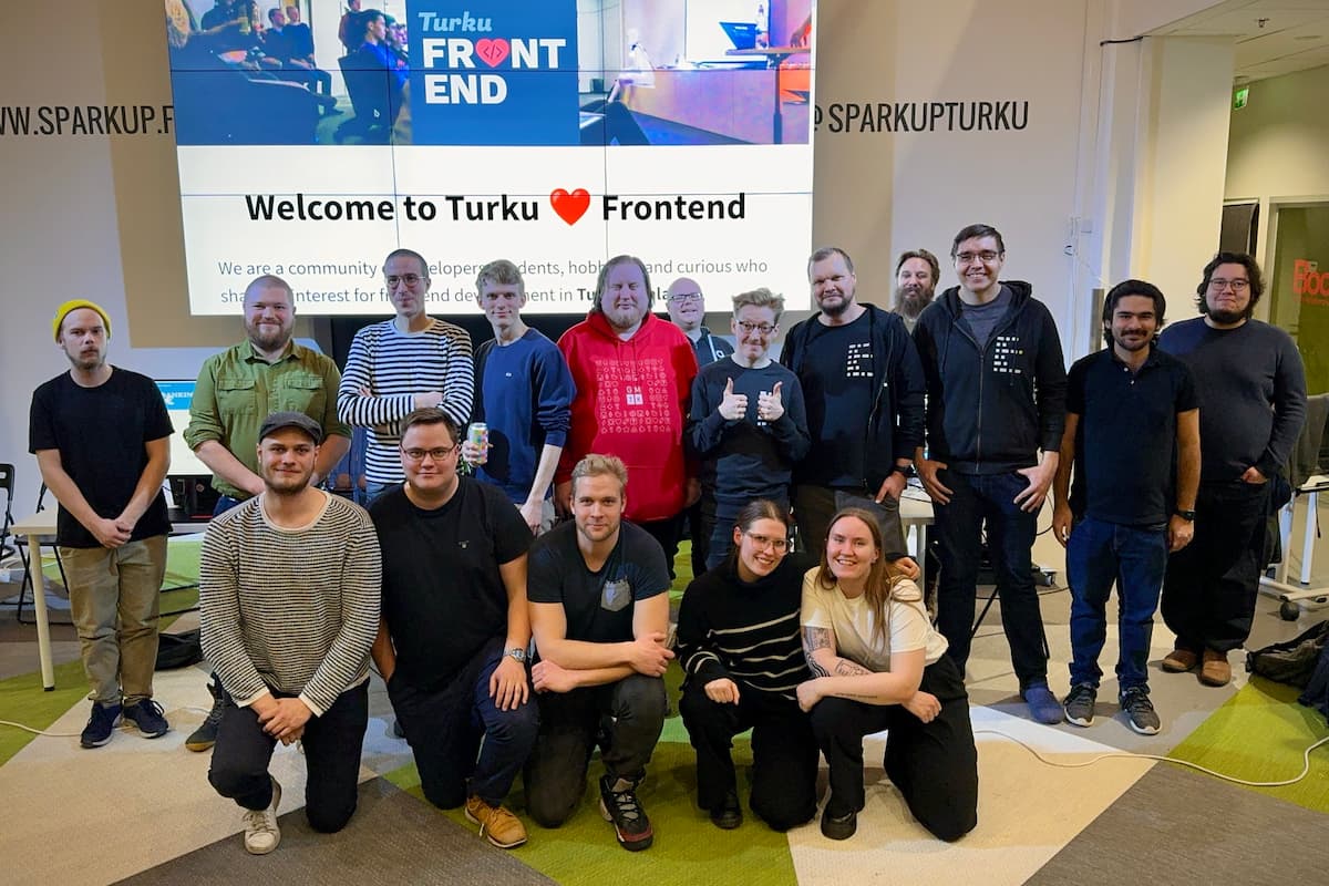 A group photo of 17 people in two rows: the participants, organizers and sponsors of Code in the Dark. Behind them, a large screen with Turku Frontend website that says “Welcome to Turku ❤️ Frontend” 