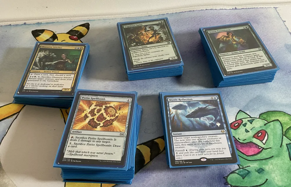 Five uneven stacks of Magic the Gathering cards in blue sleeves face up. 