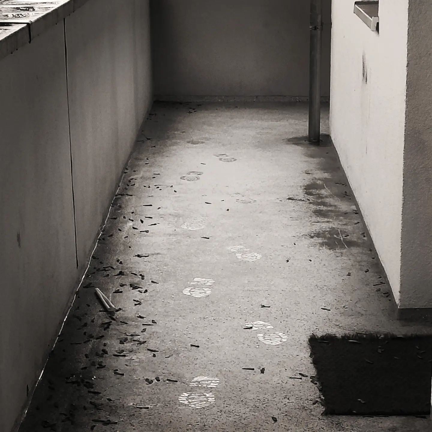 A greyscale photo of a wet concrete floor with bright footprints coming towards the camera 