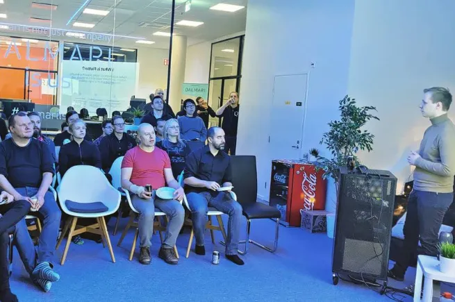 A room full of people sitting in chairs, listening to a man speak in front of the audience.